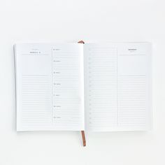 an open planner book sitting on top of a white table next to a brown pen