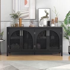 a living room with a black cabinet and pictures on the wall next to potted plants