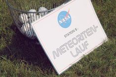 a metal basket filled with golf balls on top of a green grass covered field next to a sign