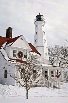 a white house with a red roof and a light tower in the background on a snowy day