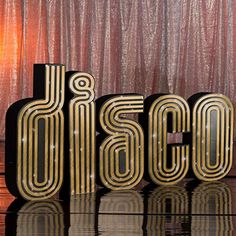 the word disco spelled out in gold letters on a black and silver surface with a red curtain behind it