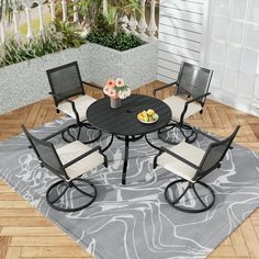 an outdoor dining set with four chairs and a table on top of a gray rug