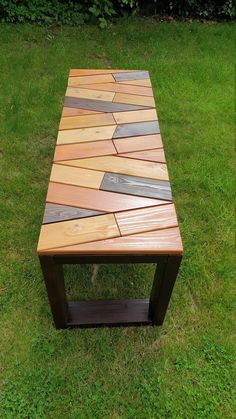 a wooden table sitting on top of a green grass covered field next to a bush