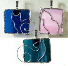 three different colored glass pendants hanging on a white wall, one with a cat and the other has a spiral design