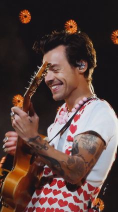 a man that is holding a guitar and smiling at the camera with flowers in his hair