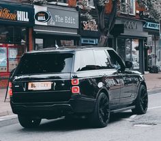 a black range rover is parked on the side of the road in front of stores