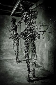 an artistic sculpture in black and white with wires wrapped around the body, standing on concrete floor