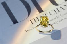 a yellow diamond ring sitting on top of a white magazine with the cover behind it