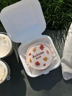 there is a cake in a plastic container on the table next to other plates and cups