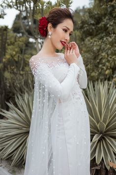 a woman in a white wedding dress standing next to a plant and wearing a flower in her hair