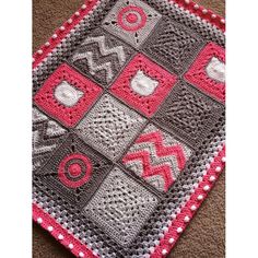 a crocheted square with pink and gray squares on it, sitting on the floor