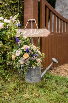 a metal watering can filled with flowers next to a wooden sign