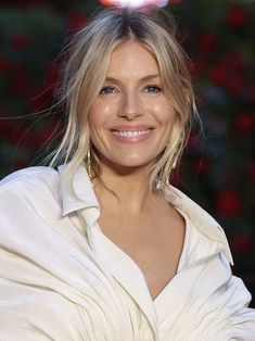 a woman with blonde hair wearing a white shirt and gold earrings smiling at the camera