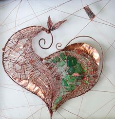 a heart shaped metal sculpture with green and red glass pieces on it's sides