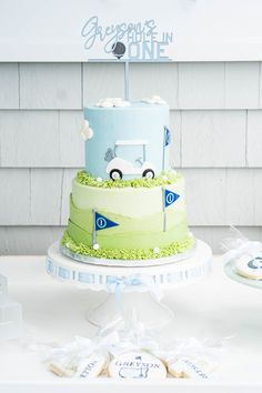 a blue and green cake on a table with cookies in the shape of cars next to it