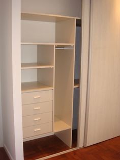 an empty white closet with drawers and shelves on the door way to another room that has a wooden floor