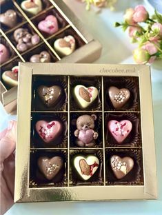 a box of chocolates with hearts and teddy bears in them on a table next to flowers