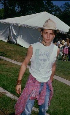 a young man wearing a cowboy hat and plaid shorts is standing in front of a white tent