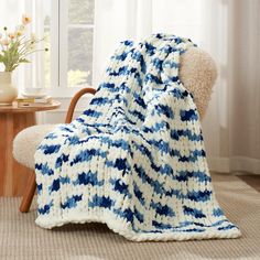 a blue and white blanket sitting on top of a wooden chair next to a window