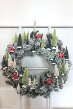 a christmas wreath hanging on the side of a door with red barns and evergreen trees