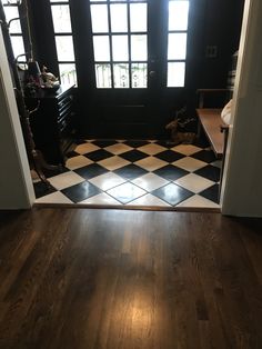 an open door leading to a black and white checkered floor in a room with two windows