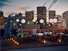 an outdoor dining set up with candles and paper lanterns in the city at night time