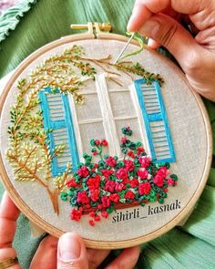 someone is stitching an embroidered wall hanging with blue shutters and flowers on it