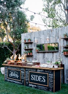 an outdoor food stand with plants and potted plants on the outside, in front of a wooden fence