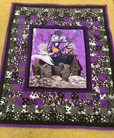 a purple and black quilted wall hanging with a skeleton holding a cake on it