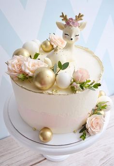 a white cake decorated with gold ornaments and pink flowers on a table next to a blue wall