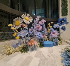 a bunch of flowers that are sitting on the ground in front of a building with glass windows