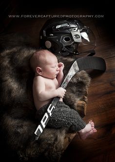 a baby laying on top of a wooden floor next to a hockey helmet