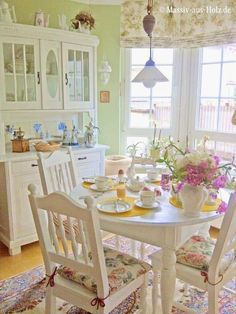 a dining room table with chairs and plates on it in front of a window filled with flowers