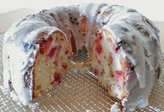 a bundt cake with white icing and berries on top sitting on a cooling rack