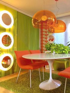 a dining room with green walls and orange chairs around a white table surrounded by plants