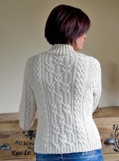 a woman standing in front of a wooden box wearing a white cable knit sweater and jeans