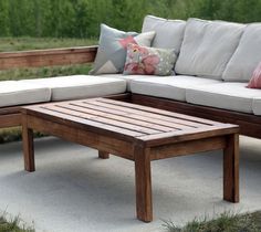 a wooden table sitting on top of a cement ground next to a couch and coffee table