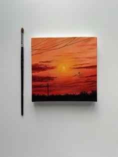 a painting with a brush next to it on a white surface and the sun is setting