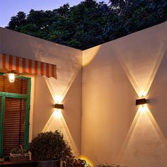 two lights on the side of a white wall next to a potted plant and window