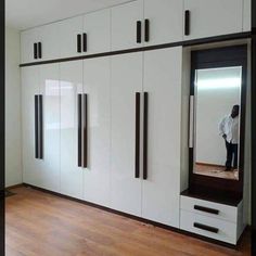 a man standing in front of a large mirror on top of a white cabinet next to a wooden floor