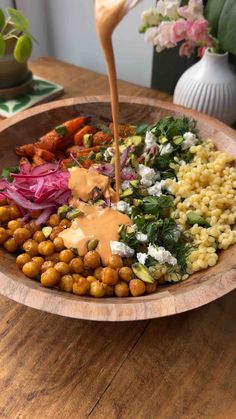 a wooden bowl filled with different types of food and dressing being drizzled over it