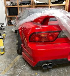 the back end of a red sports car in a garage with plastic covering it's hood