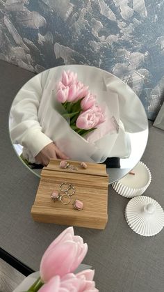 a person holding flowers in front of a mirror with jewelry on the table next to it