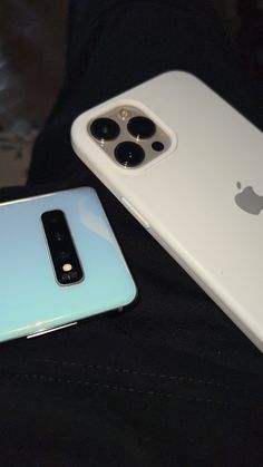 two iphones sitting next to each other on top of a black cloth covered surface