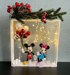 two mickey and minnie mouse figurines in front of a christmas tree with lights