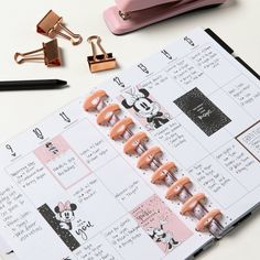 an open planner with pink clips attached to it and some other items on the table