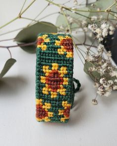 a crocheted green and yellow bracelet sitting on top of a table next to flowers