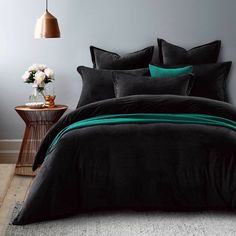 a bed with black and green comforters in a room next to a table with flowers on it