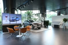 a car showroom with two cars on the screen and three chairs in front of them