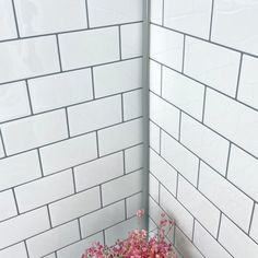 pink flowers are in the corner of a white tiled shower